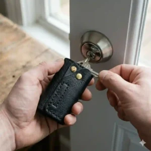 A person using a sleek leather key holder to unlock a front door, highlighting its easy one-handed operation.